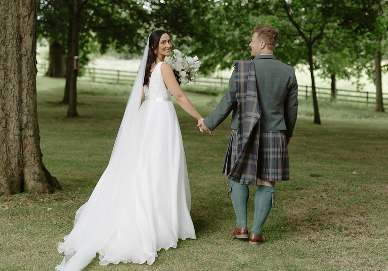 Bride and groom walking away holding hands with bride looking back to camera